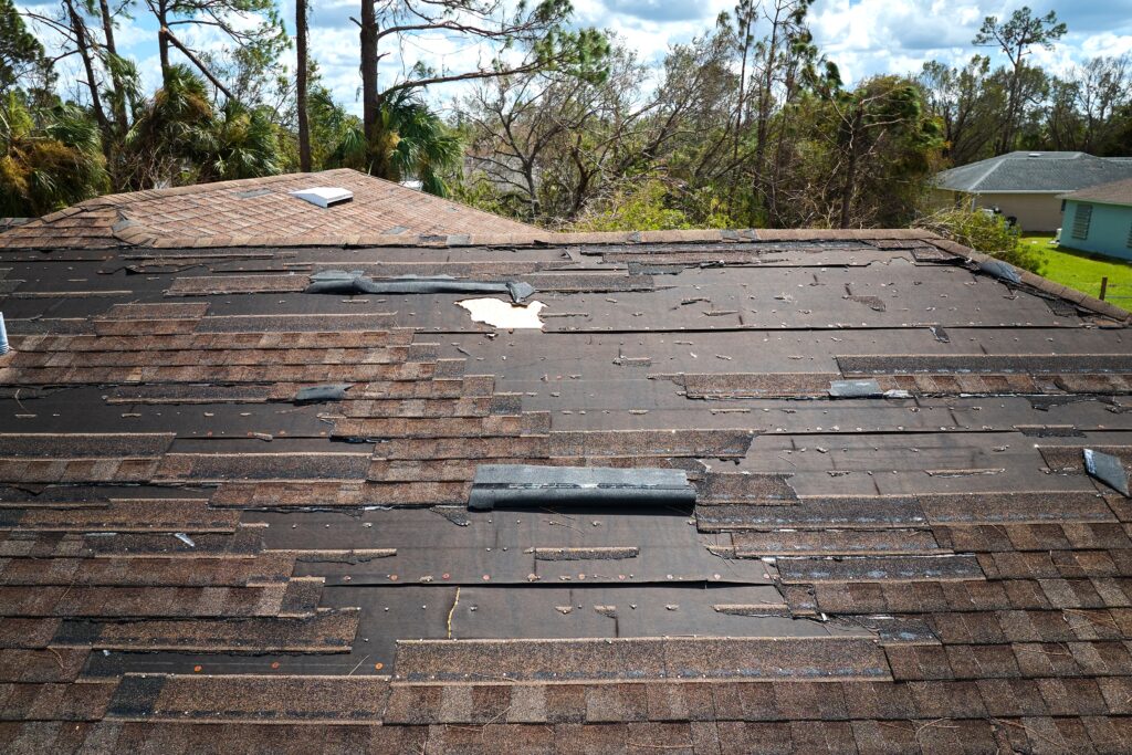 A damaged roof with missing shingles and exposed underlayment after a storm.
